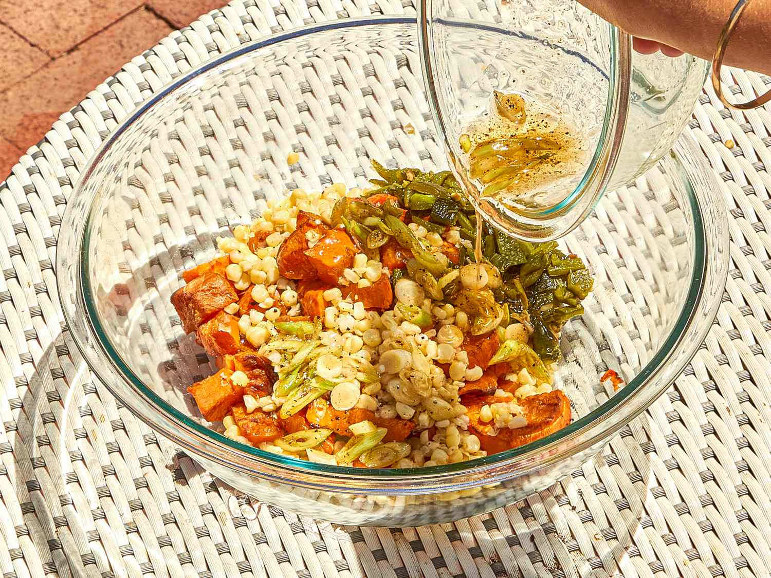 A bowl of salad with grilled sweet potatoes corn and chopped greens being dressed with vinaigrette