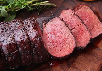 Slices of rare beef tenderloin in wooden cutting board next to fresh herbs.