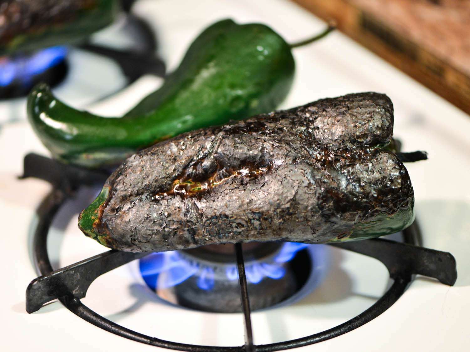 Close of green chile pepper charring directly over the flame of a stove burner