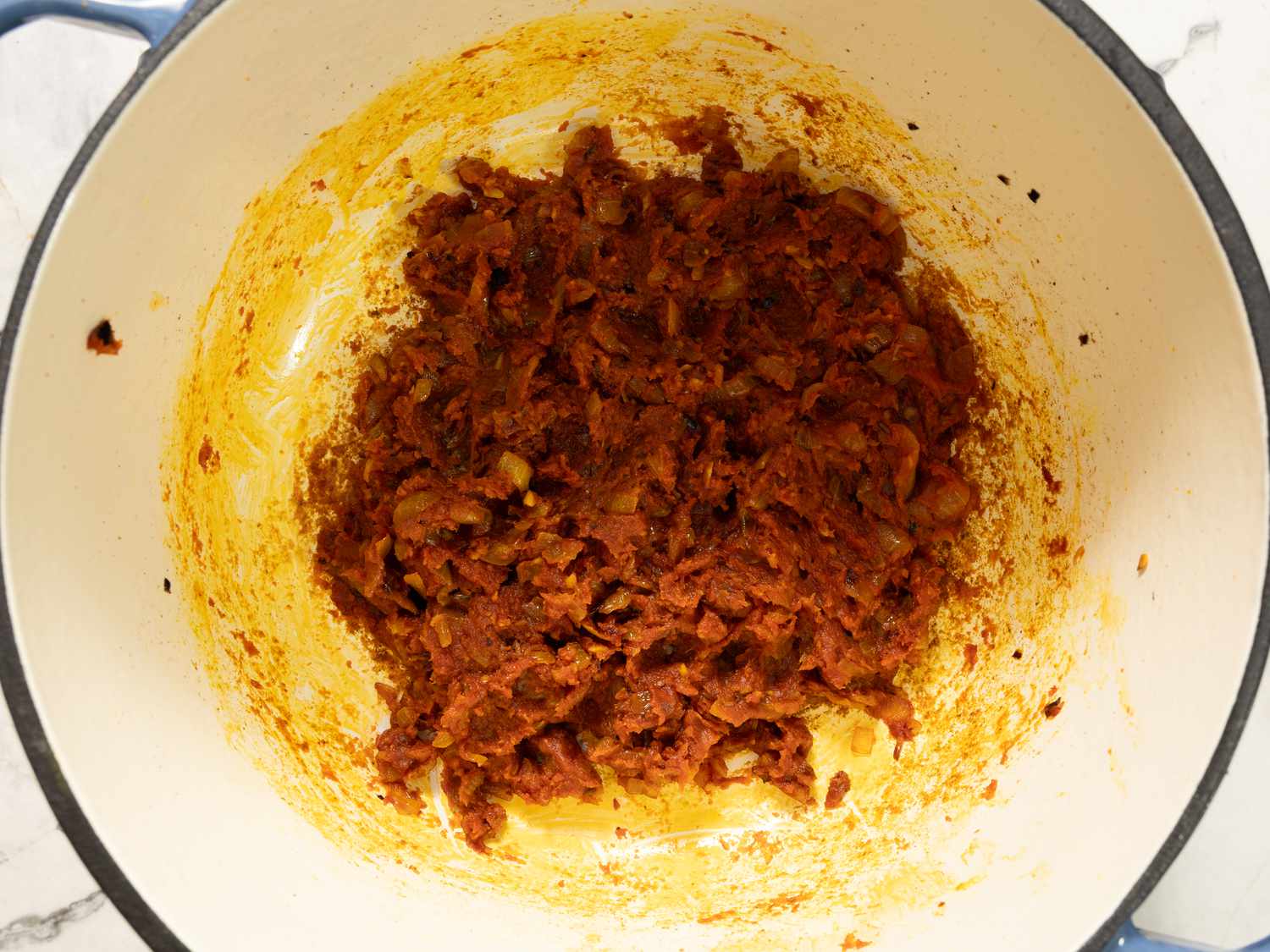 A pot containing a partly cooked mixture, with ingredients resembling minced meat or vegetables coated in a red sauce