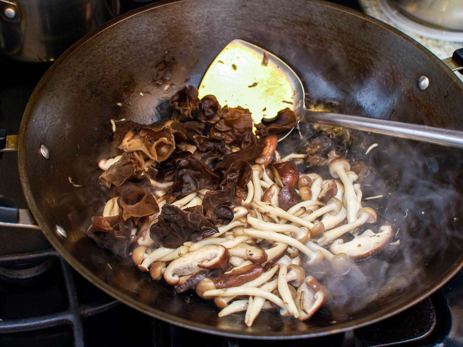 Rehydrated wood ear mushrooms are added to the fresh mushrooms in the wok.