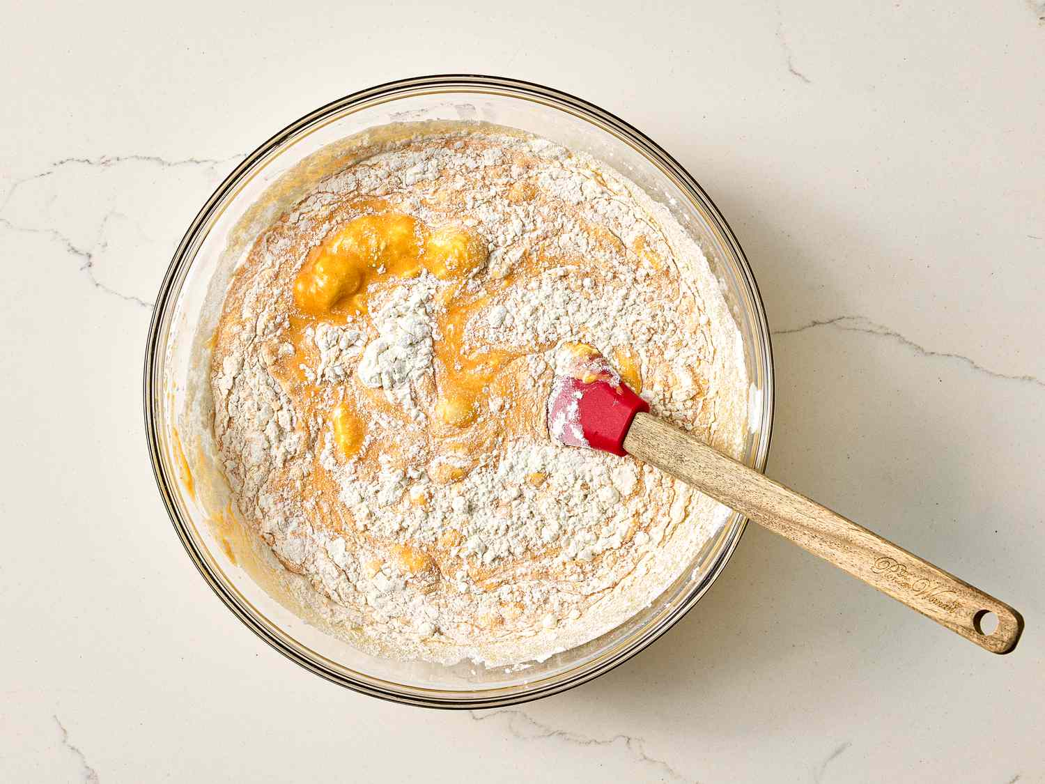 Mixing bowl with batter being prepared for a carrot cake, wooden spatula inside