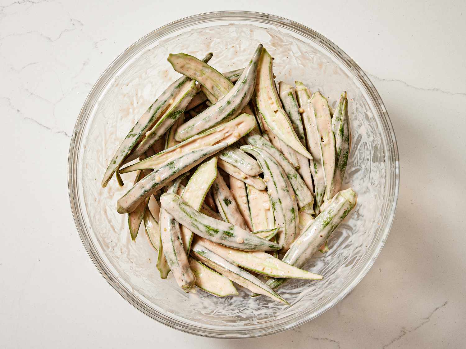 Okra tossed in a buttermilk mixture in a glass bowl 