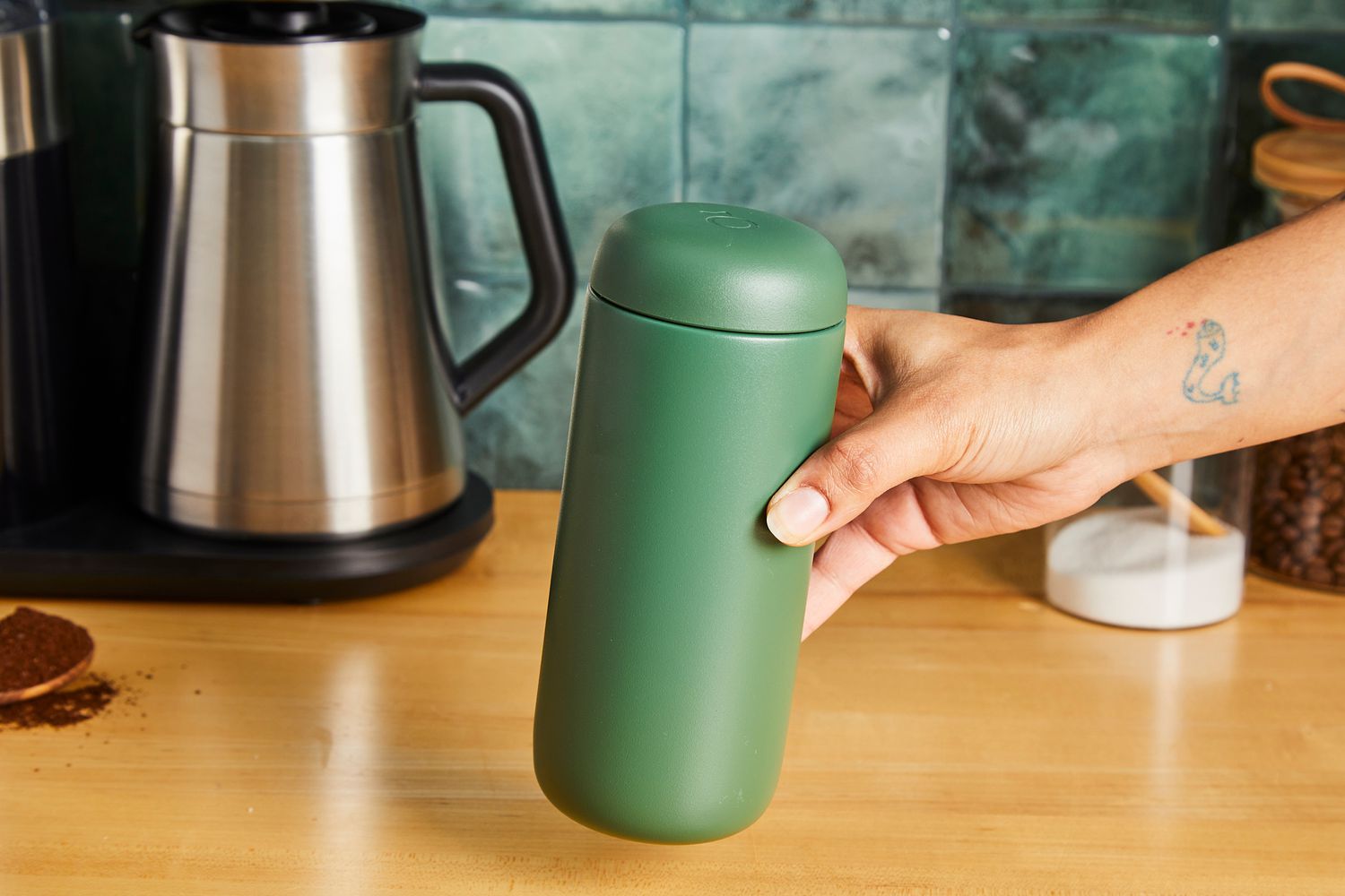 A person picking up a green Fellow travel mug.