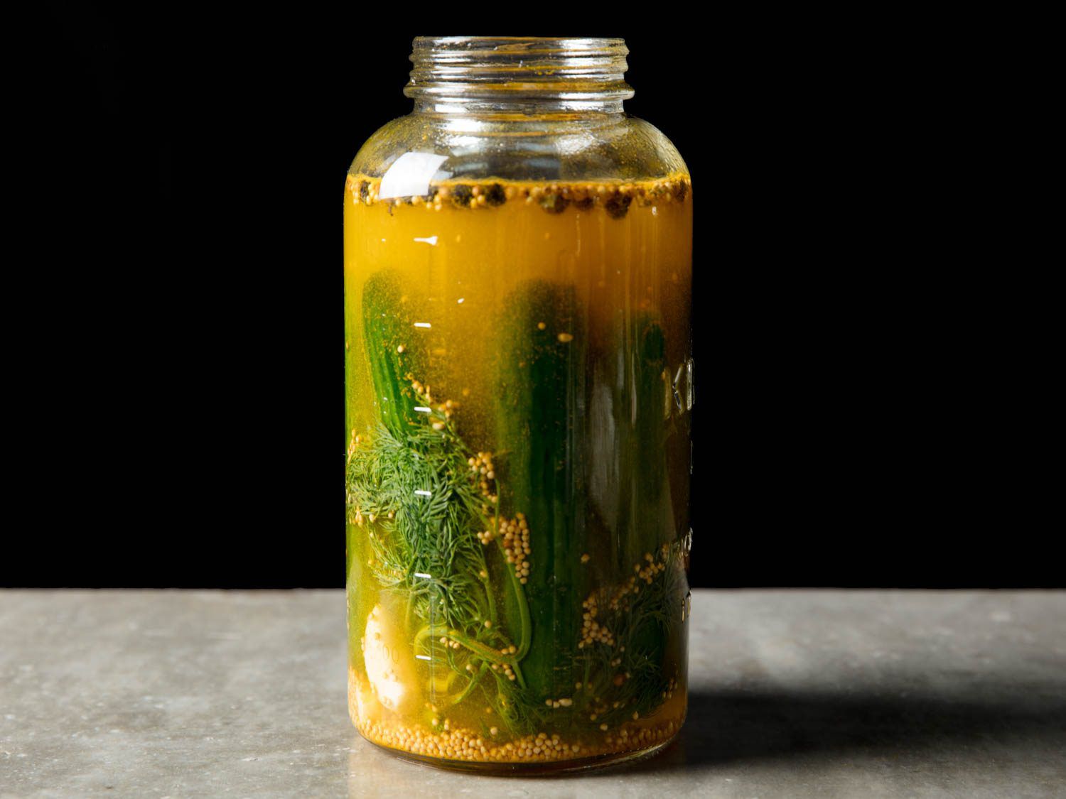 Open jar of homemade pickled cucumbers in brine, viewed from side.