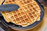 A waffle is removed from the Cuisinart WMR-CANAS Round Classic Waffle Maker