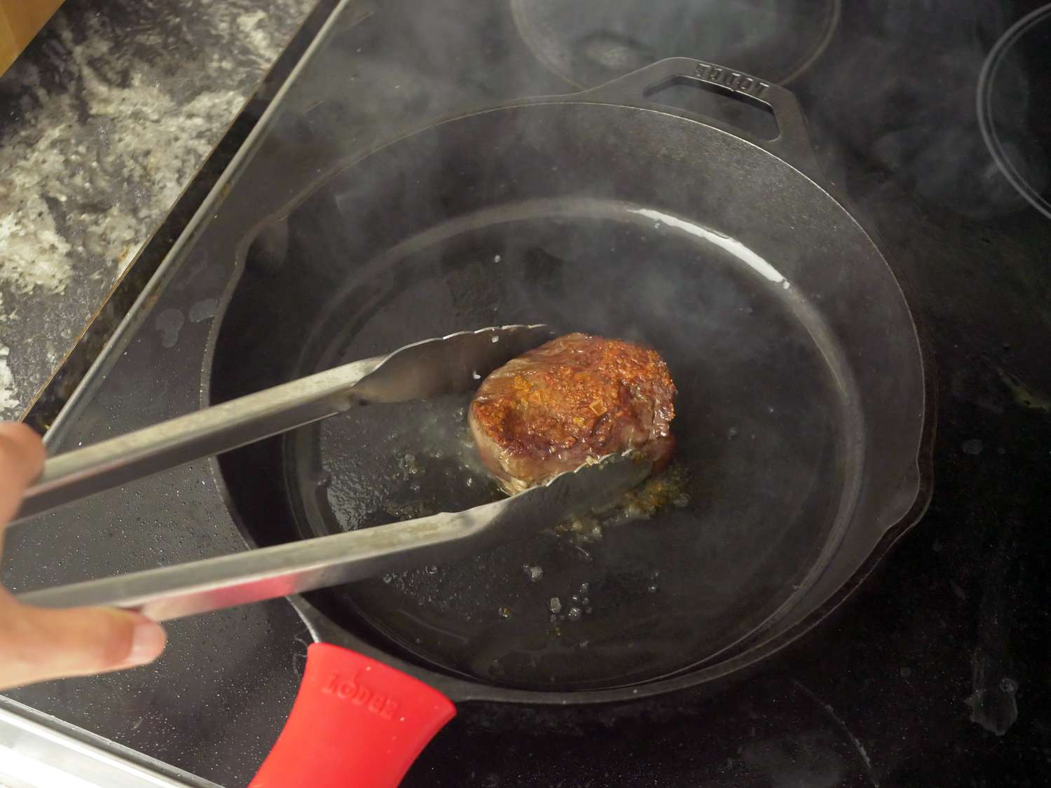 a person flipping steak in a lodge skillet