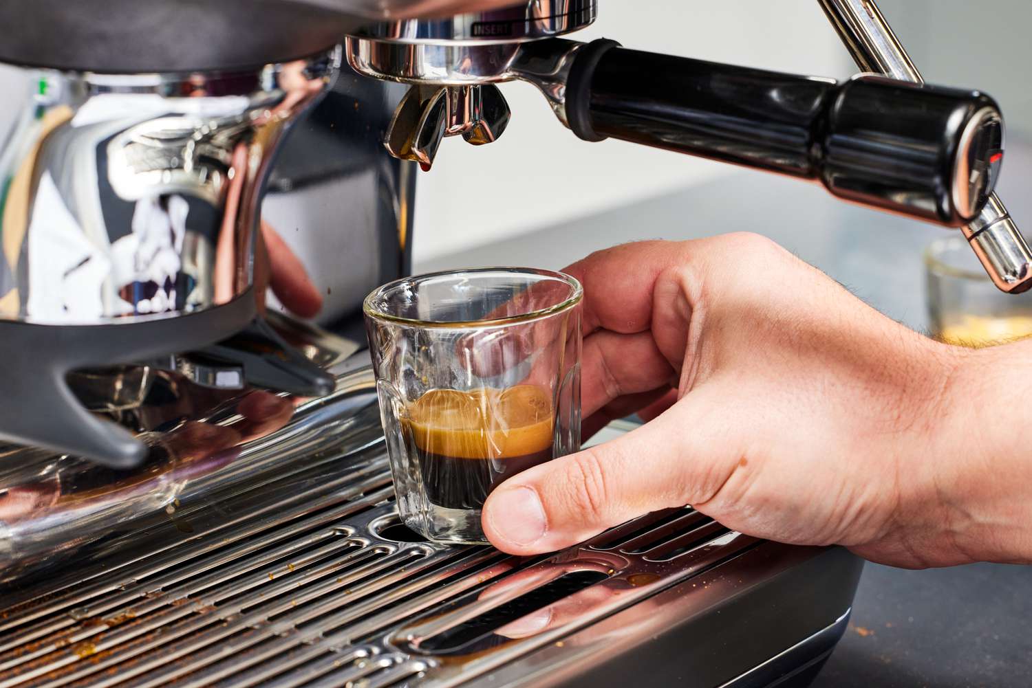 A person adjusting an espresso cup on the tray of the Breville The Barista Touch Impress