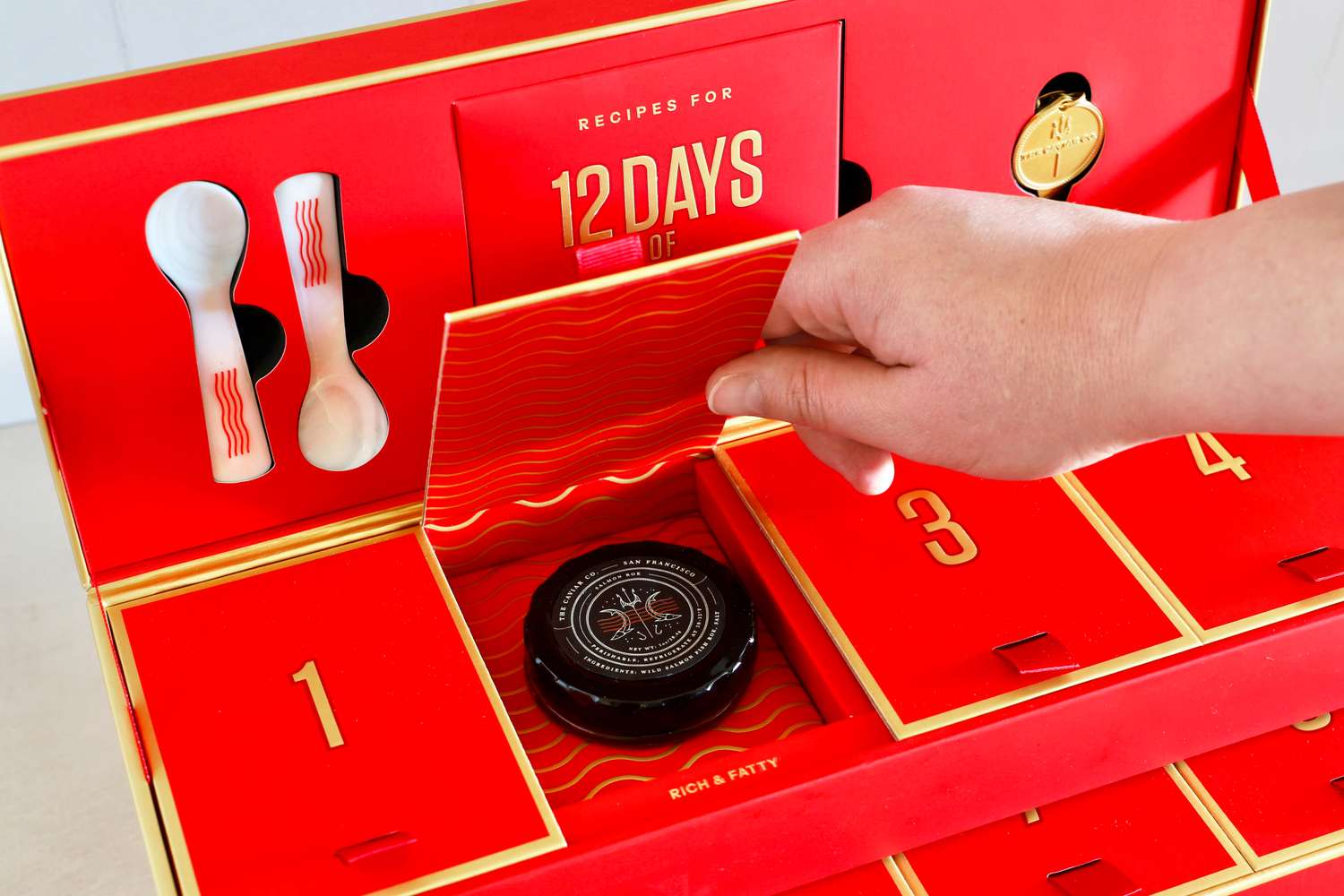 A hand opening a door on the Caviar Co 12 Days of Caviar Advent calendar to reveal a jar of salmon roe