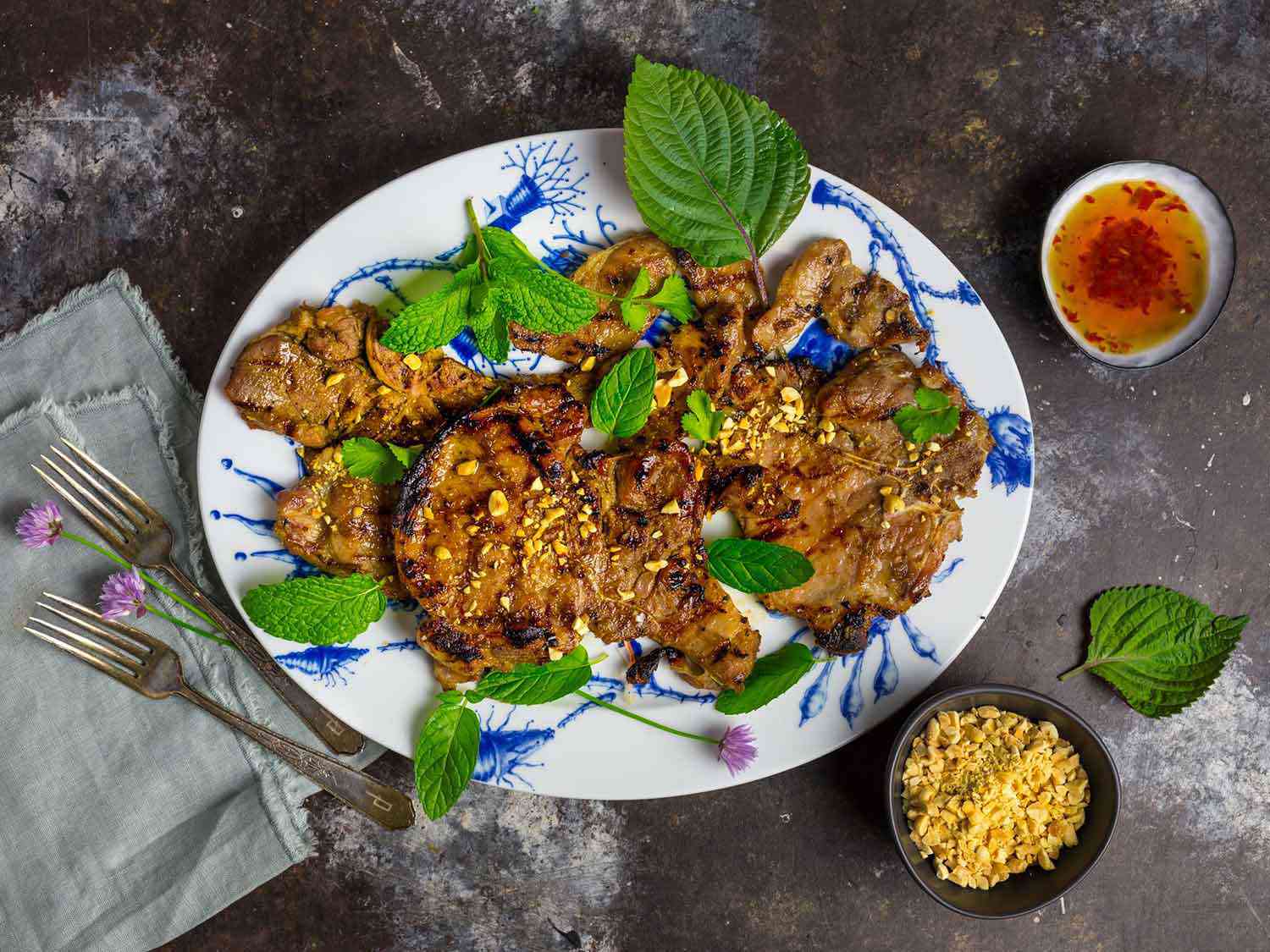 A platter of the Vietnamese grilled pork chops, garnished with herbs and flanked by bowls of nuoc cham and crushed peanuts.