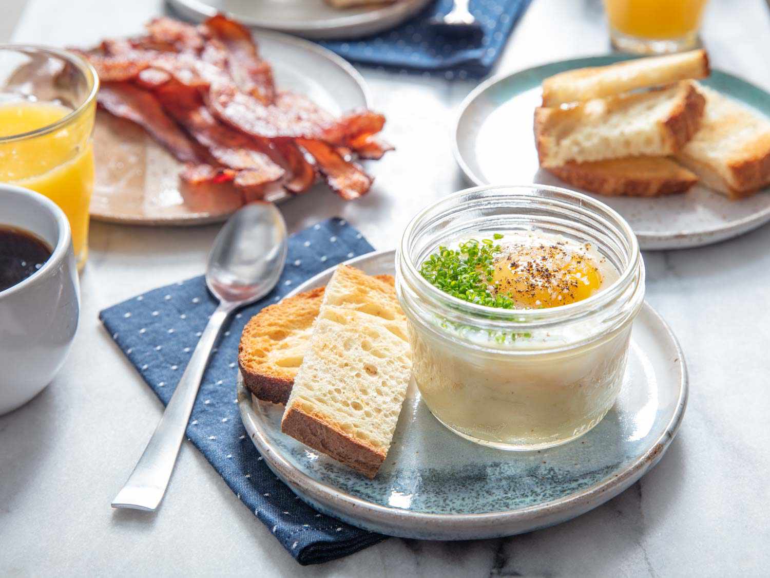 Plated mason jar of mashed potato topped with a sous-vide cooked egg, served with toast bread and bacon.