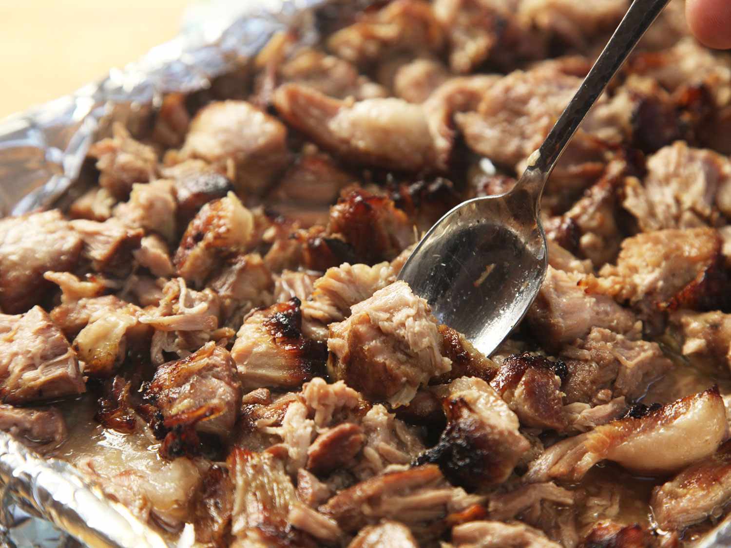 Shredded sous vide pork carnitas on a foil-lined baking sheet after broiling to crisp.