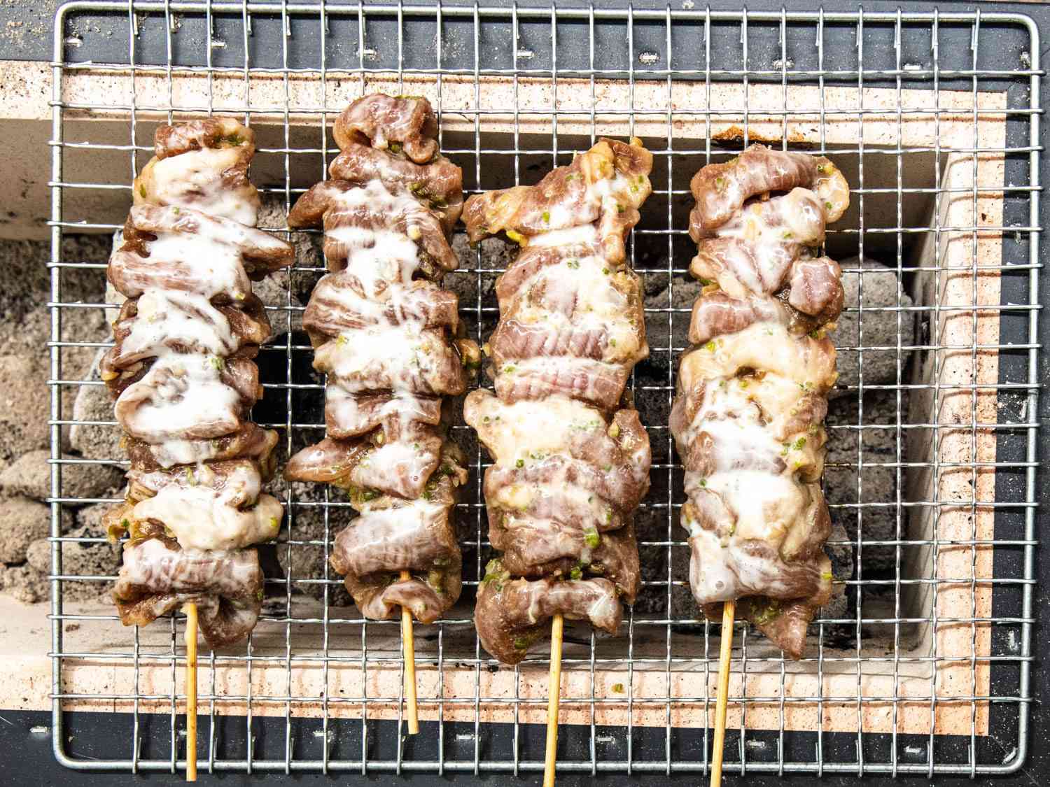 Overhead closeup of Thai pork skewers grilling on a Japanese konro grill.