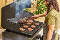 A person cooks meat in the Weber Genesis E-325 Liquid Propane Gas Grill
