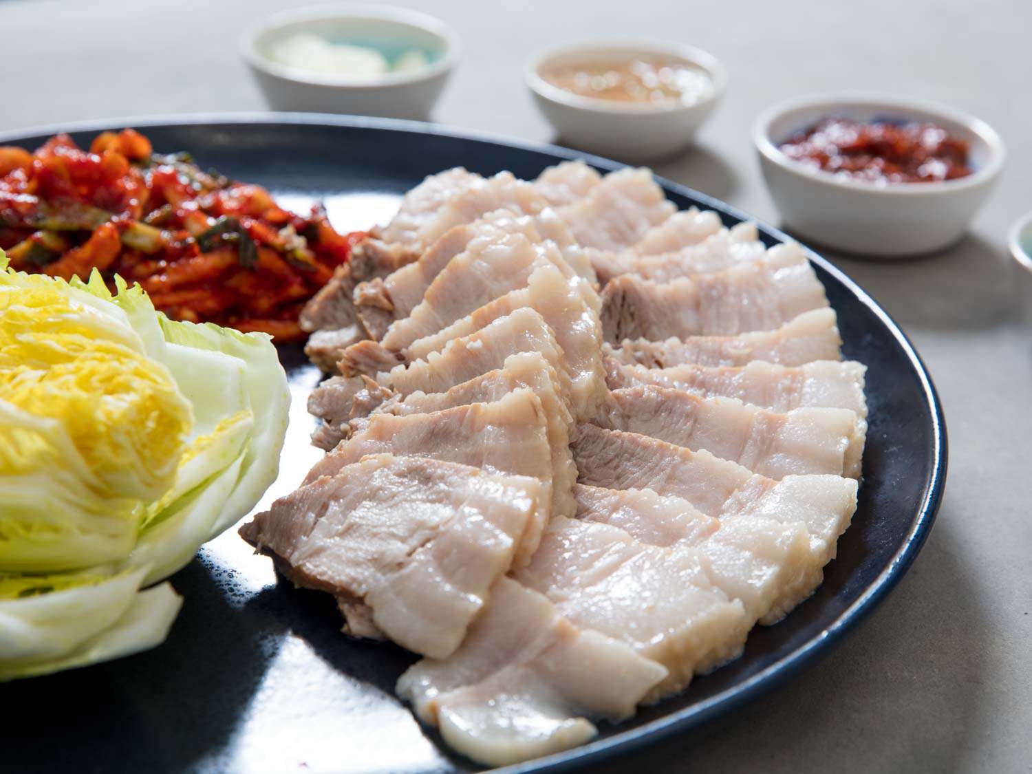 A platter of bossam featuring pork belly, brined cabbage, and spicy radish. 