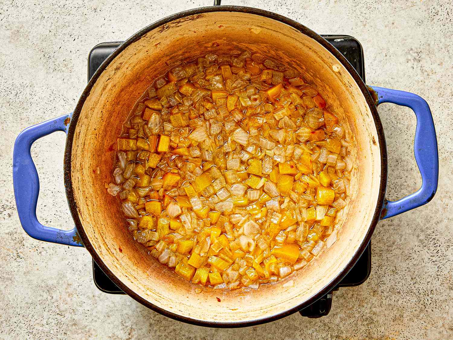 Cooking pot with a mixture of chopped onions and yellow vegetables partway through the preparation of a dish