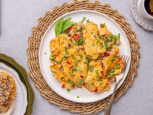 A plate of a prepared Nigerianstyle omelet garnished with herbs accompanied by a bagel and a cup of tea on a woven mat