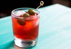 A Campari Spritz in a rocks glass, garnished with 3 olives on a pick. 