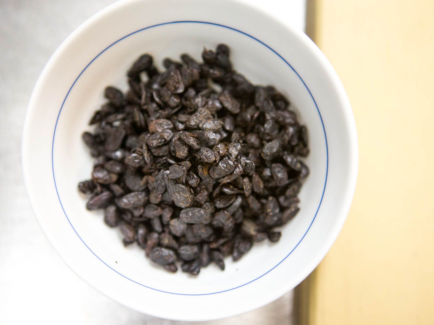 Fermented black soy beans in a white bowl with a blue line.