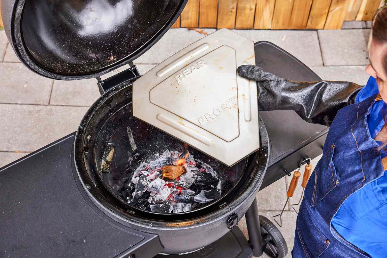 A person places a heat deflector inside the Char-Griller Akorn Auto-Kamado Grill