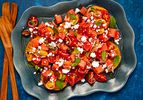 A dark bowl with tomato-watermelon salad, sprinkled with mint and feta, 