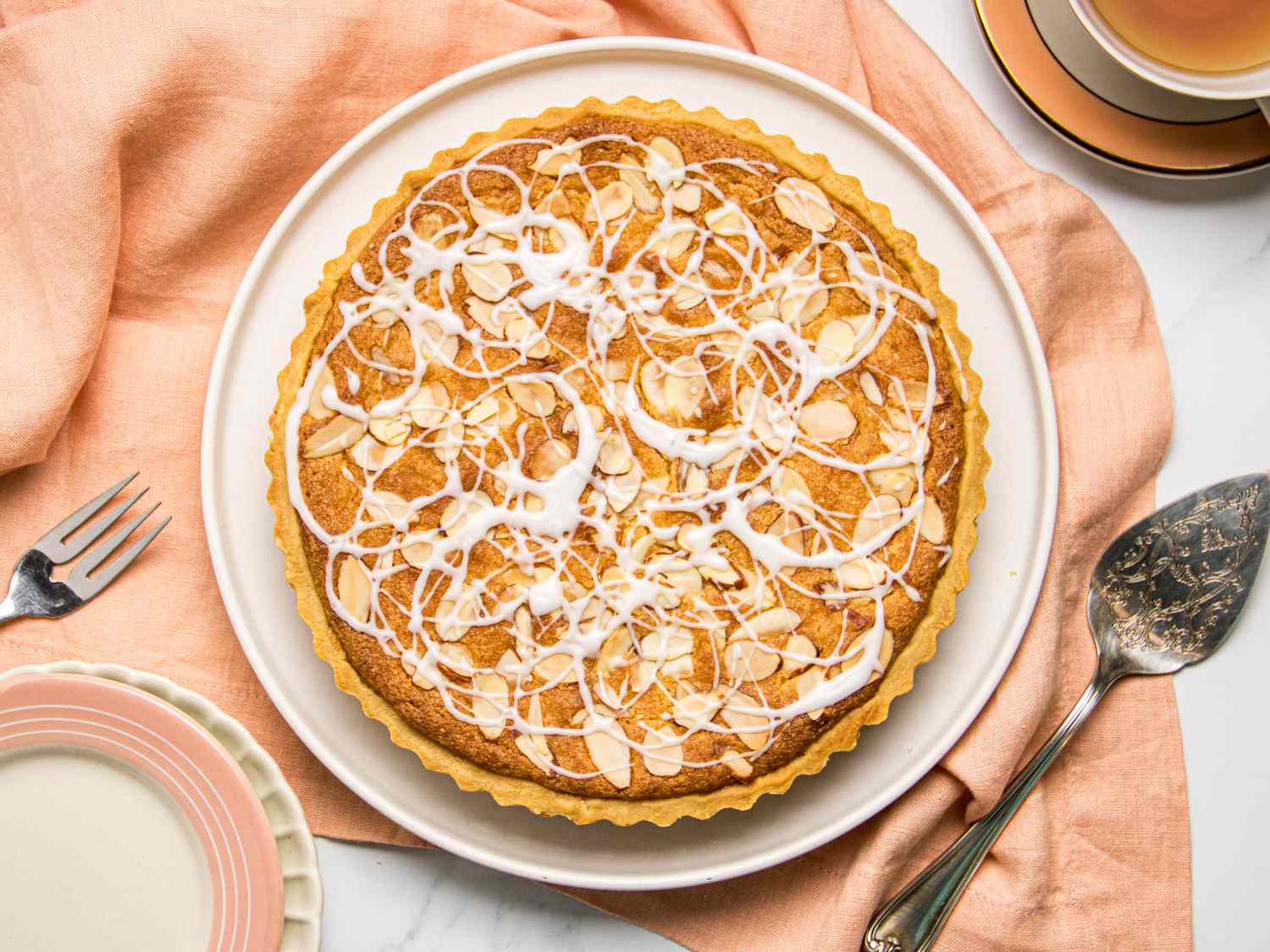 A decorated bakewell tart served on a plate with cutlery beside it