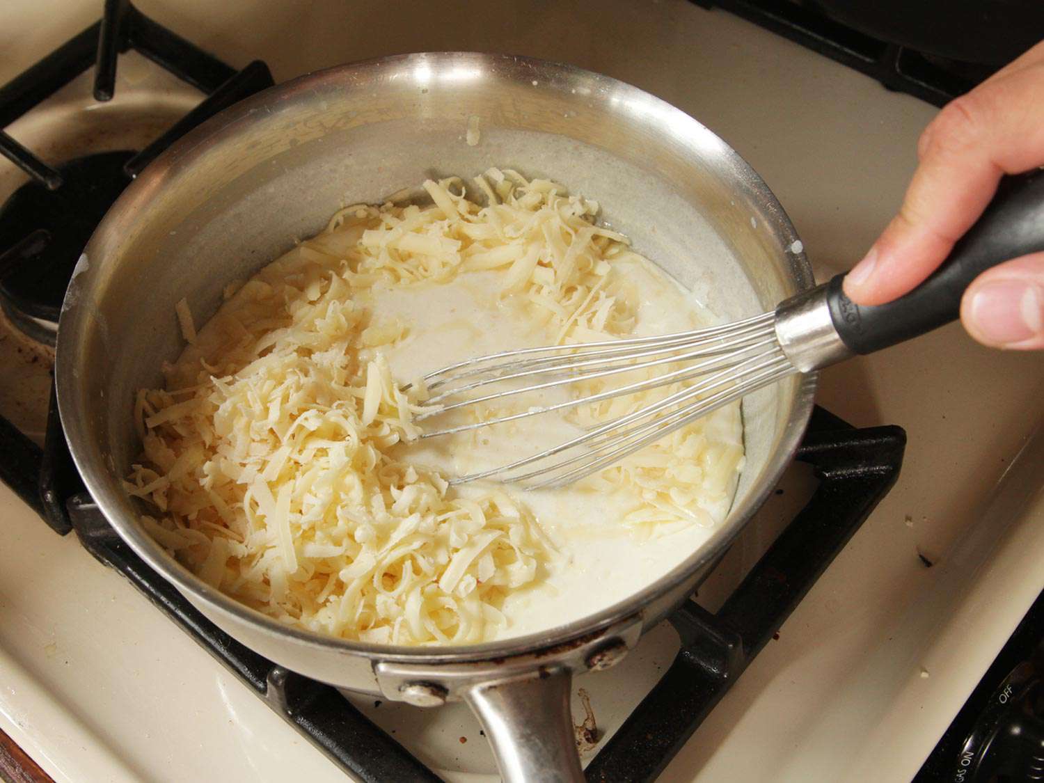 Whisking gruyere cheese in a saucepan of white sauce. 