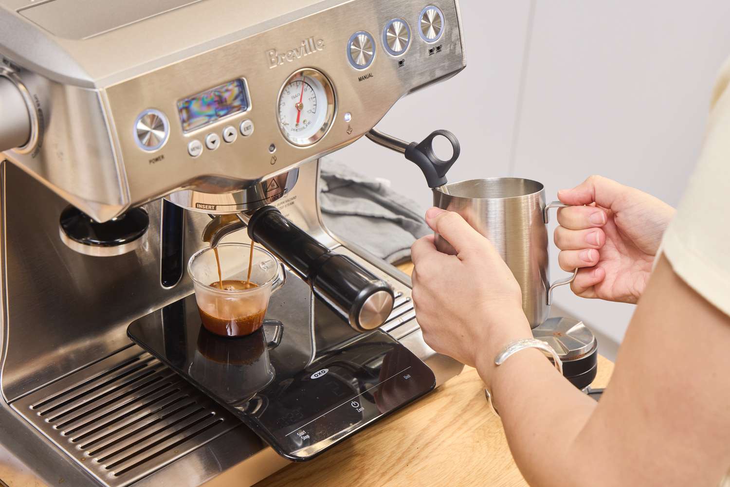 A person makes a cappuccino using the Breville BES920XL Dual Boiler Espresso Machine