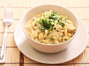 Green chile chicken mac and cheese, served in a white bowl and garnished with scallions and cilantro.