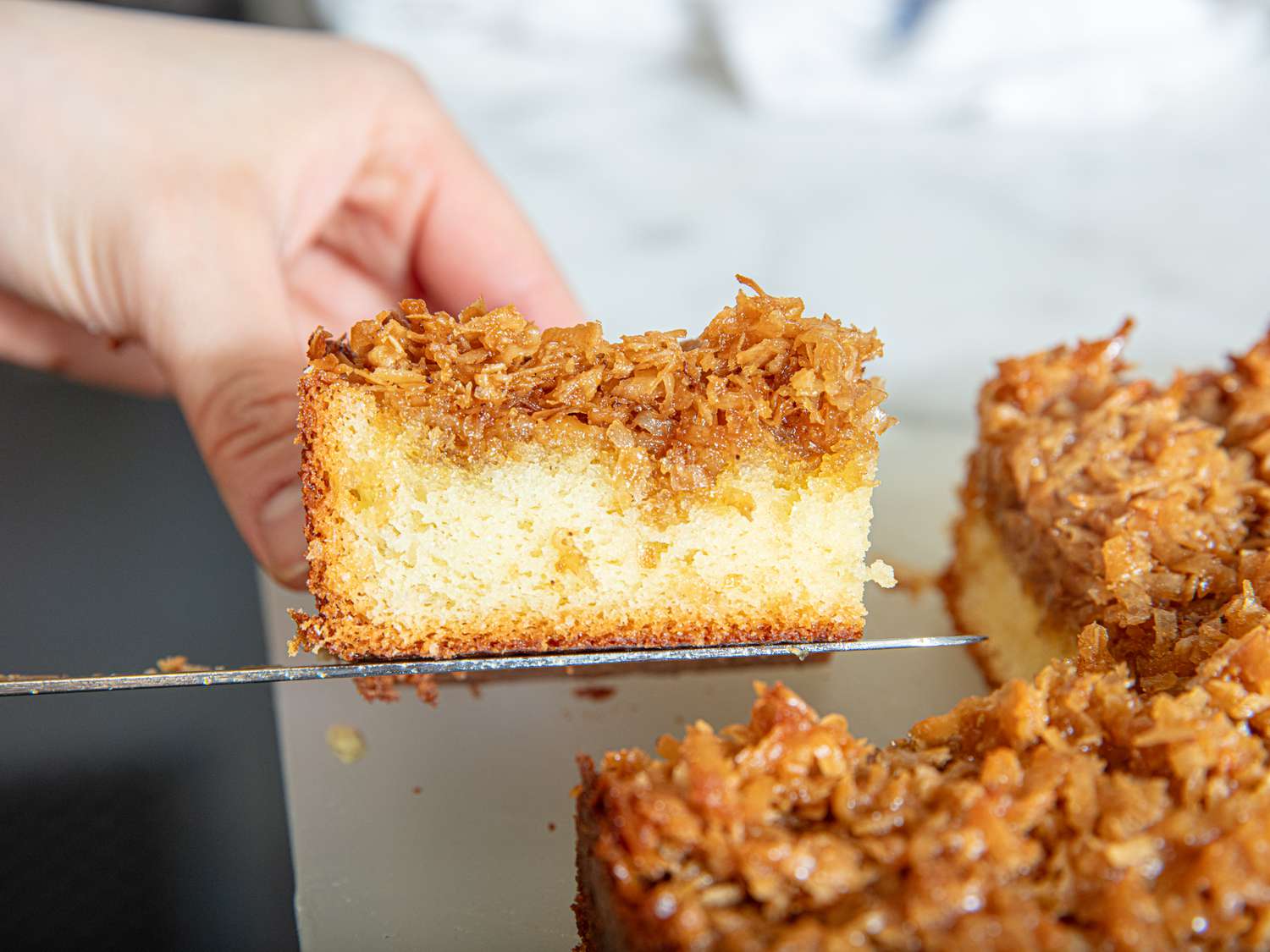 A slice of cake with a crunchy topping being lifted from the tray