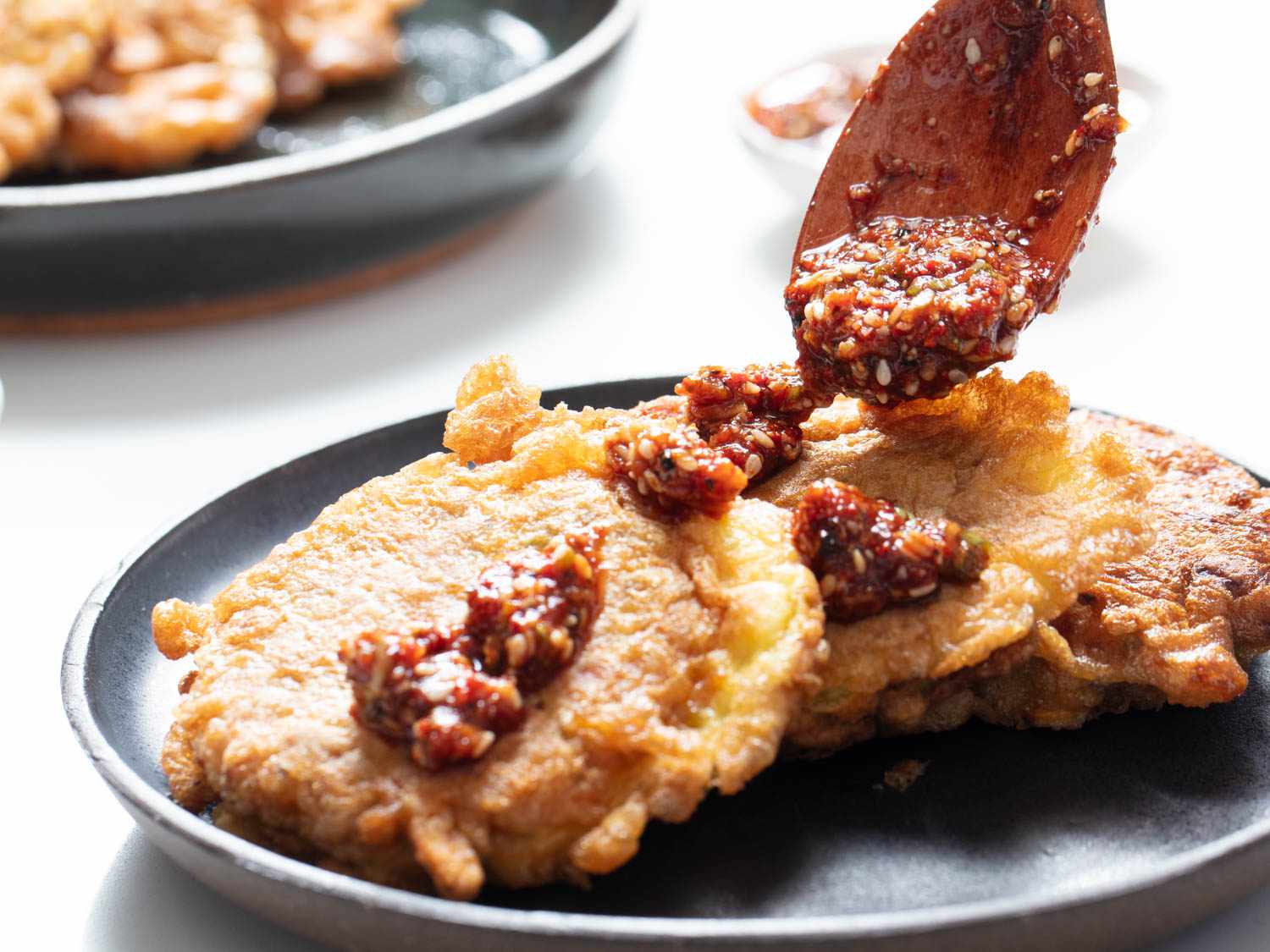Spooning Korean yangnyeom sauce over jeon pancakes