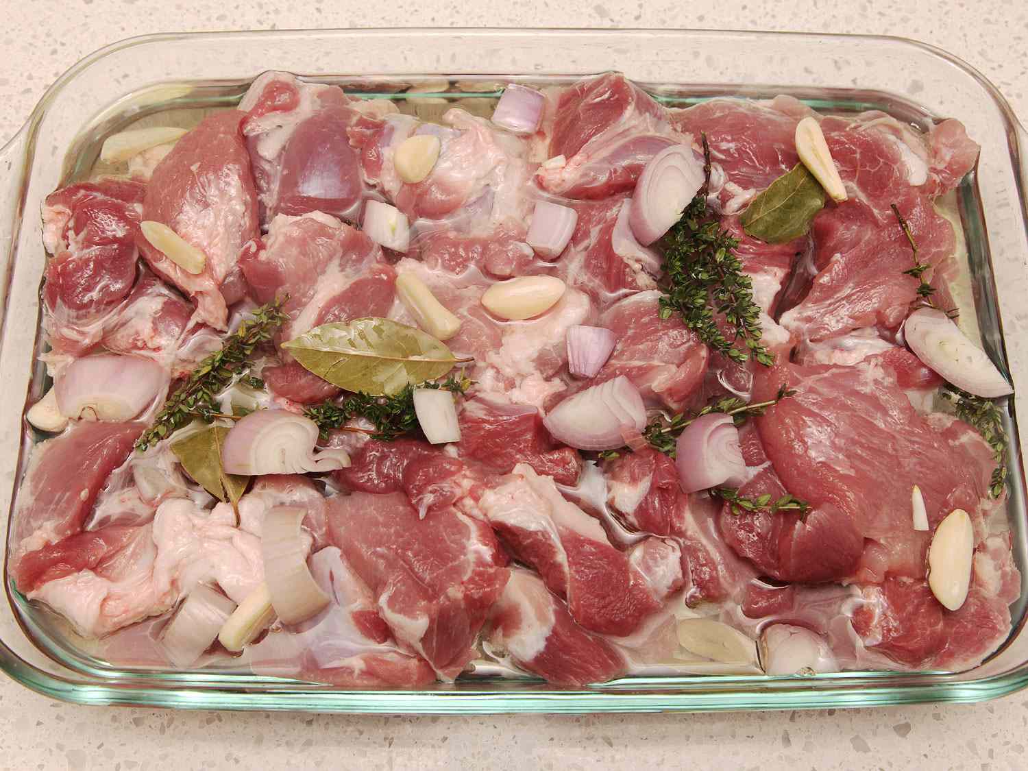 Pork, shallots, garlic, and herbs are tightly packed in a baking dish and partially submerged in lard.