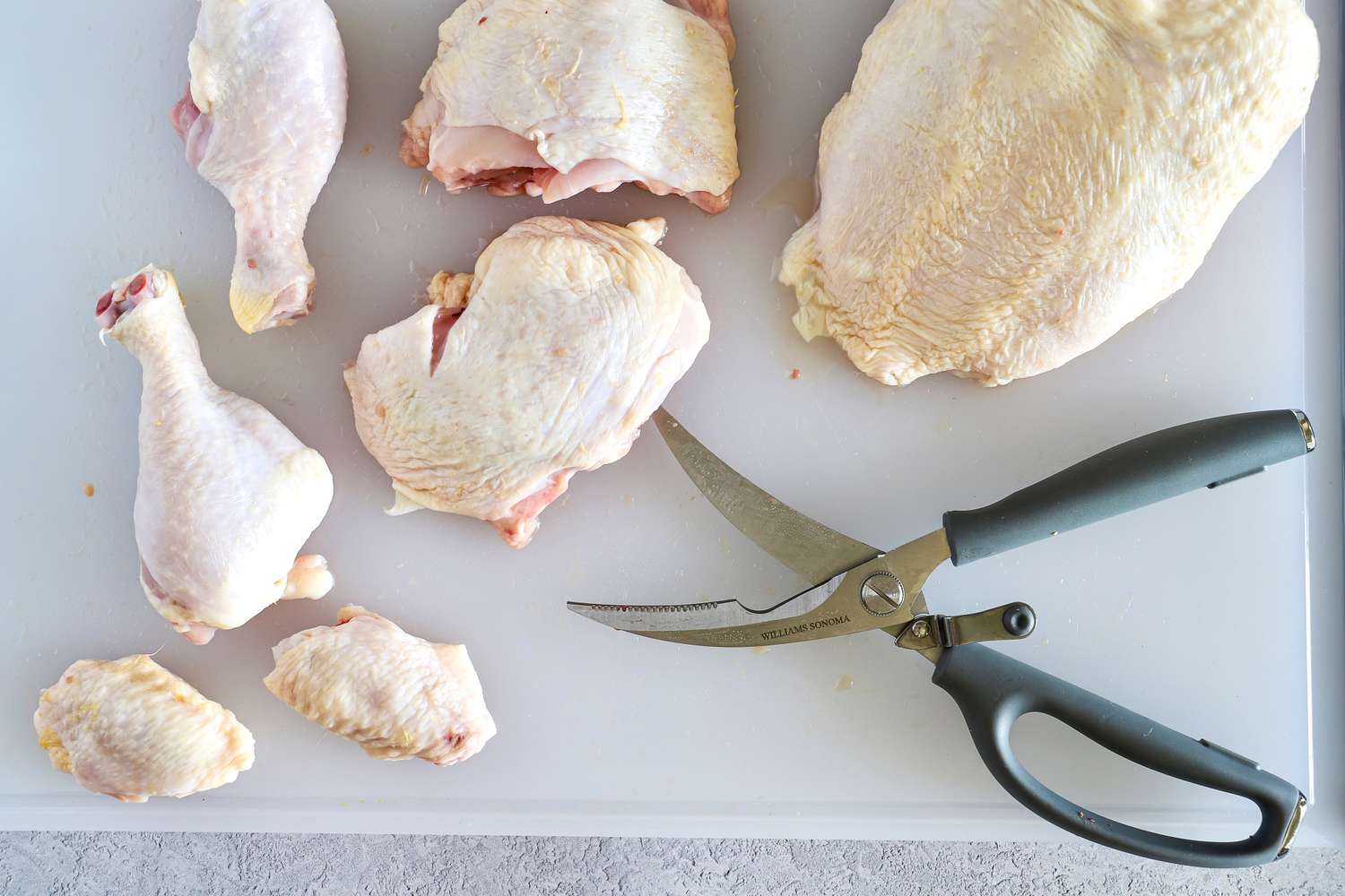 Raw chicken pieces on a cutting board with Williams Sonoma poultry shears