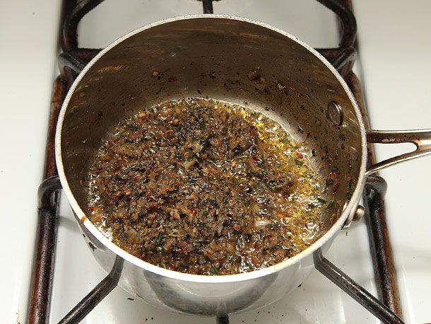 The finished seasoning mixture of garlic, shallots, rosemary, lemon zest, chile flakes, and anchovy cooked down in a saucepot for roast boneless leg of lamb in a saucepan.