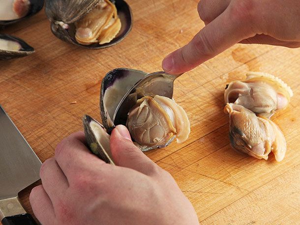 Removing cooked clam from shell with a spoon.