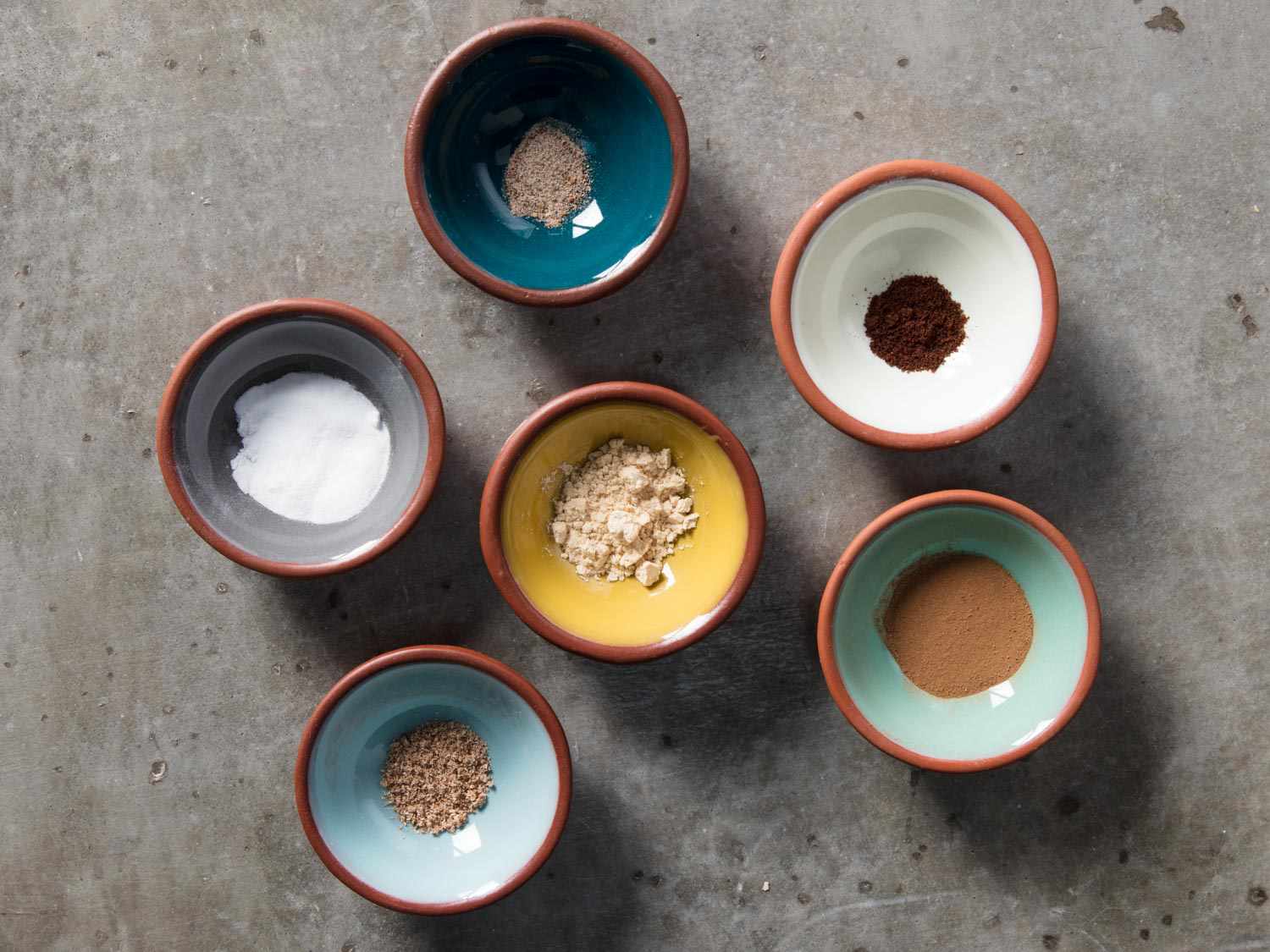 Six small bowls holding various ground spices. 