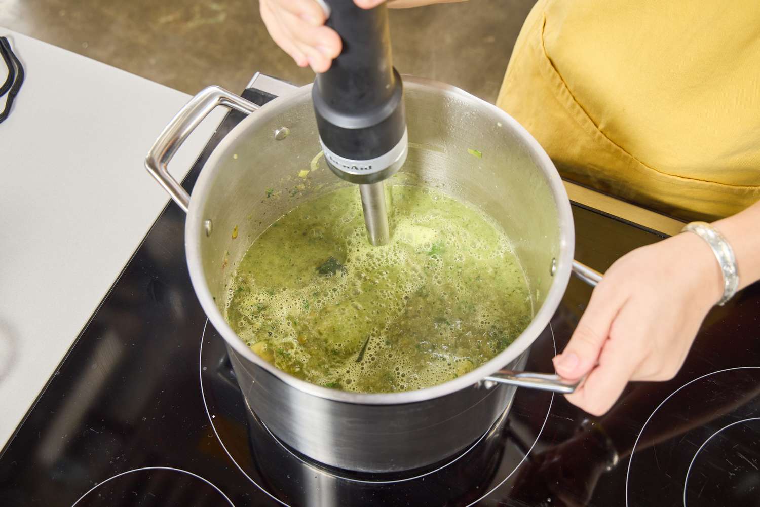 A person uses the KitchenAid Go Cordless Hand Blender to make soup