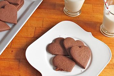 A white plate and platter piled high with gluten-free spicy hot chocolate cookies. Glasses of milk are close at hand.