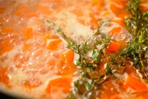 Carrots simmering in stock with thyme sprigs.