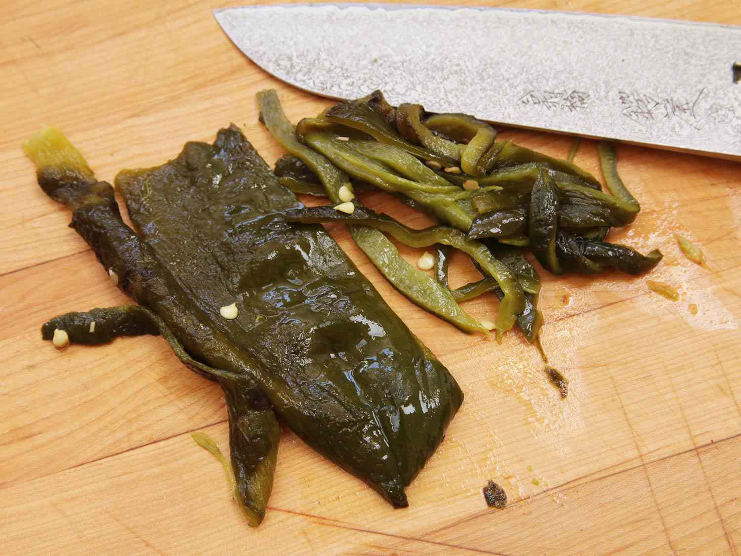 Strips of green roasted poblano pepper on cutting board board next to chefs knife