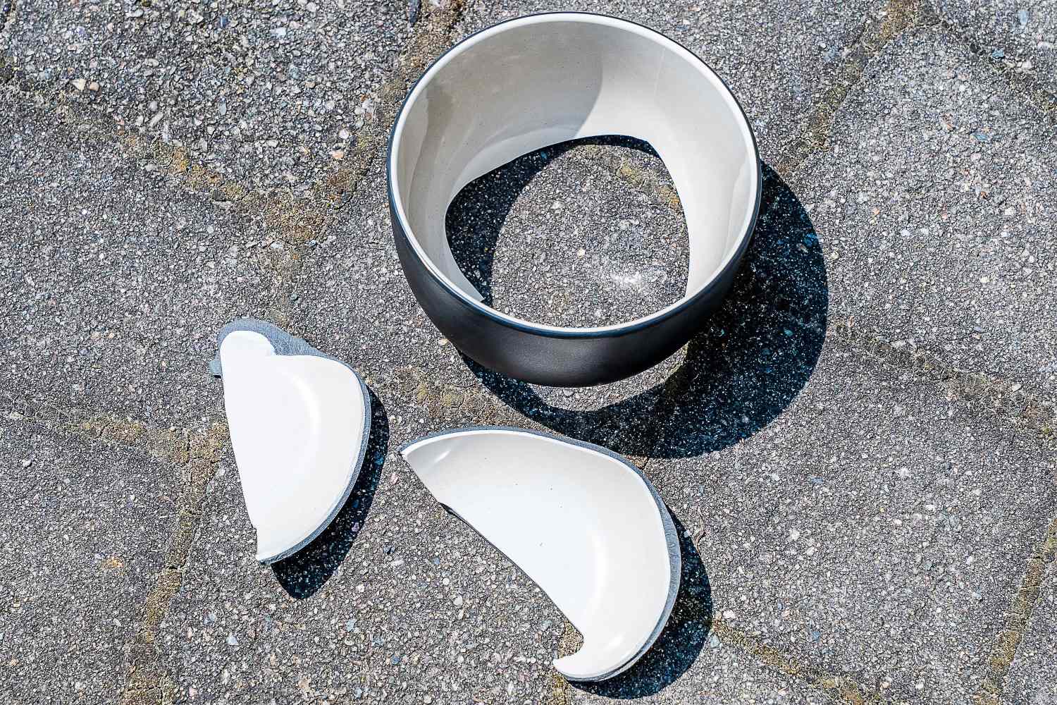 Three pieces of a broken outdoor dinnerware bowl on a stone patio