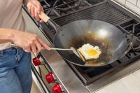 A person fries an egg in the Mammafong Pre-Seasoned Blue Carbon Steel Flat-Bottom Pow Wok