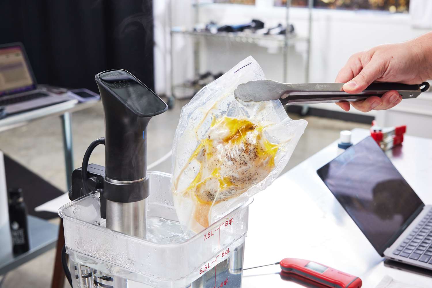 Hand using tongs to remove food packet from water set up with the Anova Culinary Precision Cooker Pro