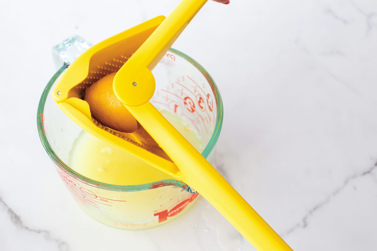A person using a lemon juicer to juice a lemon into a measuring cup.