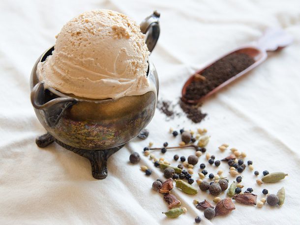 A scoop of chai flavored ice cream in a small teapot, alongside whole spices.