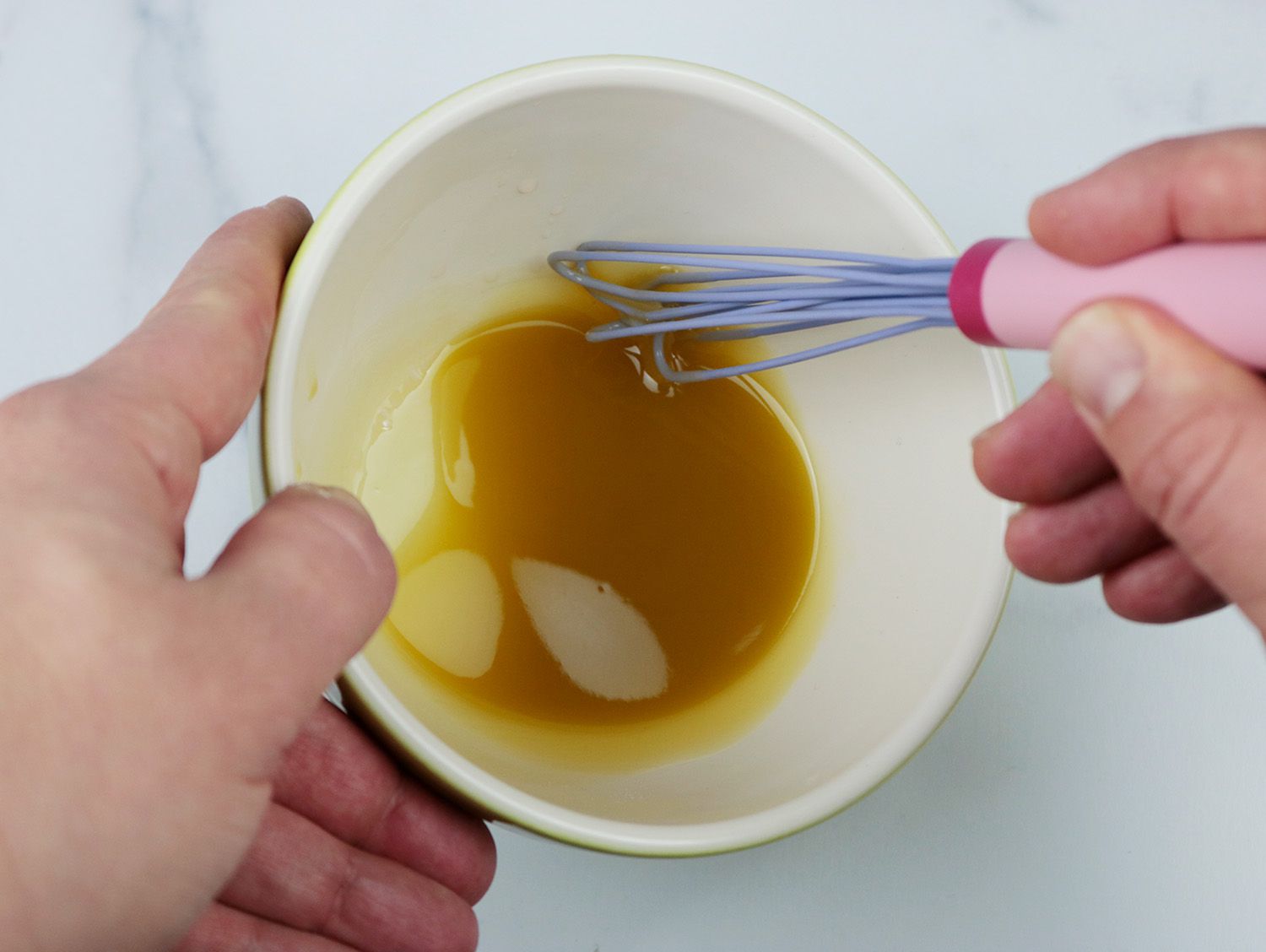 a silicone coated mini whisk emulsifying a vinaigrette in a ceramic bowl