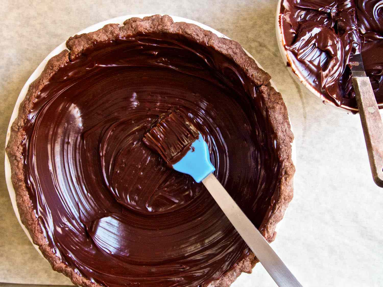 Spreading chocolate caramel sauce inside a pie crust with a brush.