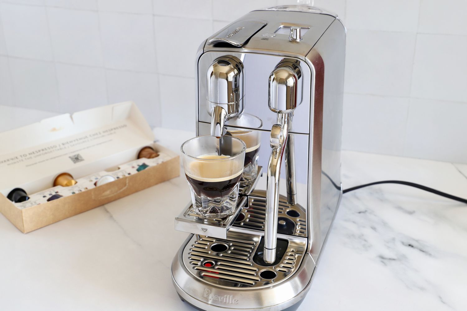 A coffee machine with a glass of coffee brewing capsules in a box next to it