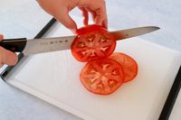 Slicing a tomato with the Tojiro F-687 Hand Made Bread Knife on a white cutting board