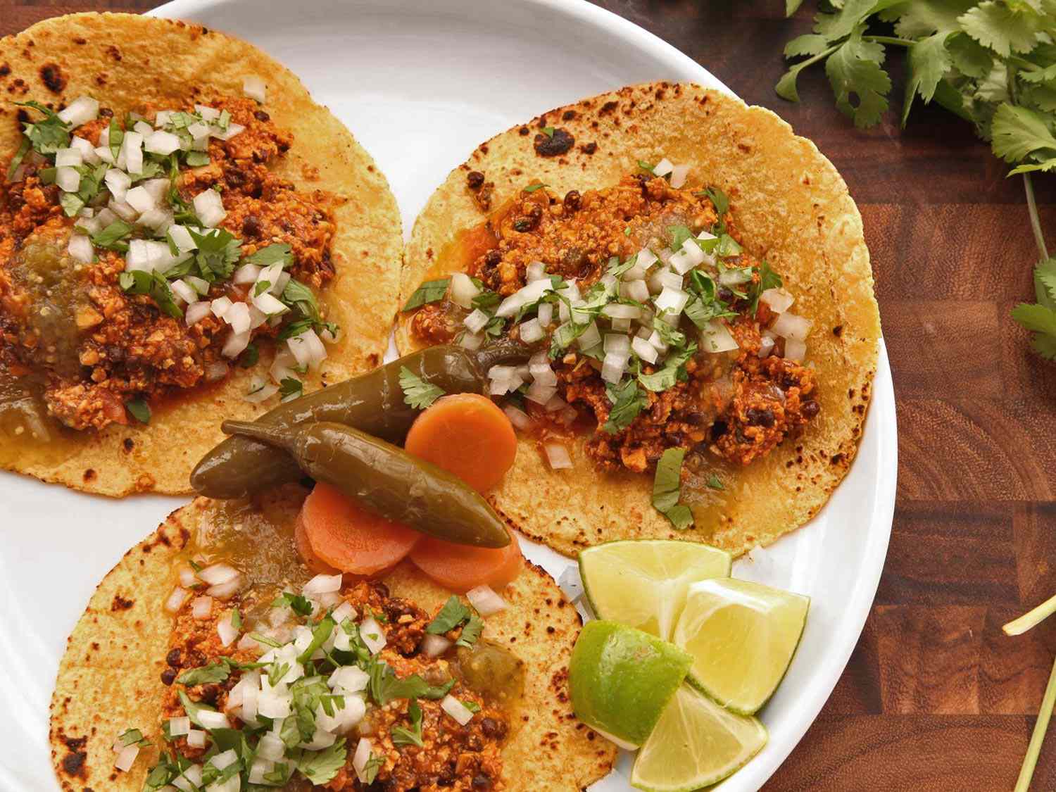 A plate of vegan chorizo tacos, garnished with pickled jalapeños and lime wedges.